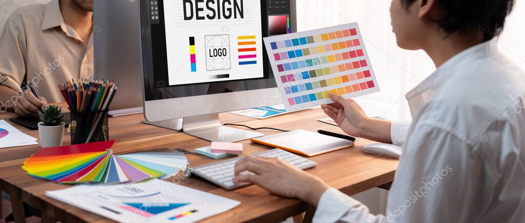 Graphic designer work on computer laptop and with graphic drawing pen while brainstorming unique design with professional graphic team in modern digital studio workplace. Panorama shot. Scrutinize