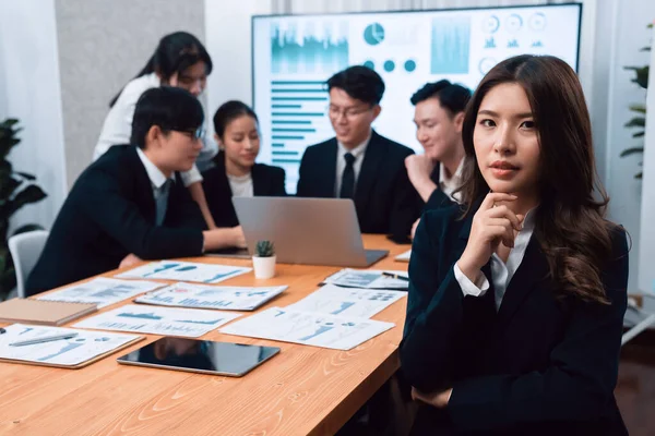 Focus portrait of female manger, businesswoman in the harmony meeting room with blurred of colleagues working together, analyzing financial paper report and dashboard data on screen in background.