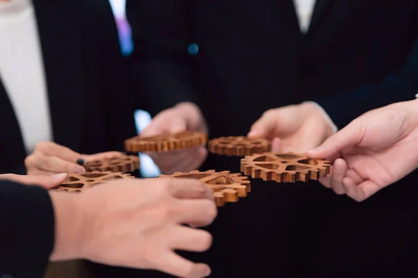 stock image Closeup hand holding wooden gear by businesspeople wearing suit for harmony synergy in office workplace concept. Group of people hand making chain of gears into collective form for unity symbol.