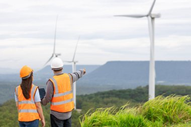 Erkek ve kadın mühendisler kırsal kesimdeki bir tepenin tepesinde ya da dağda rüzgar çiftliğinde çalışıyorlar. Yenilenebilir ve sürdürülebilir enerjinin gelecekteki üretimi için yenilikçi idealler.