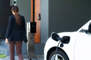Progressive woman install cable plug to her electric car with home charging station. Concept of the use of electric vehicles in a progressive lifestyle contributes to clean environment.