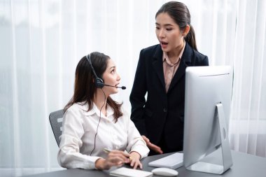 Kulaklık takan Asyalı bayan müşteri destek operatörü onun destekleyici menajeri tarafından yönlendirilir. Tecrübeli meslektaşım, bir müşteri ile görüşmeyi yürüten operatöre yardım ediyor, tavsiye ve rehberlik sağlıyor. Coşkulu.