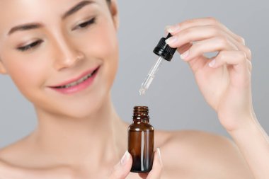 Focus cannabis extracted oil bottle with dropper lid holding by blurred glamorous beautiful asian woman with perfect clean skin and soft smooth makeup in isolated background.