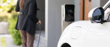 İlerici kadın elektrikli arabasının fişini şarj istasyonuna takıyor. İlerici bir yaşam tarzında elektrikli araç kullanımı kavramı temiz çevreye katkıda bulunur.