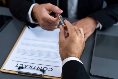 İş anlaşması yapılırken iki işadamı masanın karşısında oturuyor. Şirket avukatı, sözleşmeyi imzalaması için müvekkiline ya da ortağına kalem veriyor ve anlaşmayı imzayla imzalıyor. Coşkulu