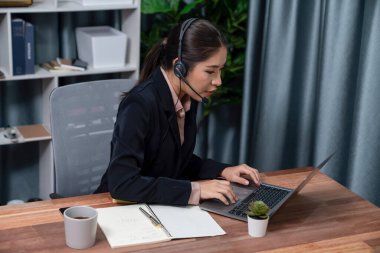 Bilgisayarında mikrofon ve kulaklıkla Asyalı çağrı merkezi çalışıyor. Kadın operatör istisnai müşteri hizmetleri sunar. Destek veren çağrı merkezi ajanı, müşteriye soruşturmada yardım ediyor. Coşkulu.