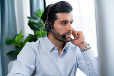 Erkek çağrı merkezi operatörü ya da telesales temsilcisi ofis masasında oturmuş kulaklık takıyor ve müşteri hizmetleri desteği sağlayan ya da satış yapan müşteriyle sohbet ediyor. coşkulu