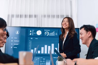 Confidence and young asian businesswoman give presentation on financial business strategy in dashboard report display on screen to colleagues in conference room meeting as harmony in workplace concept