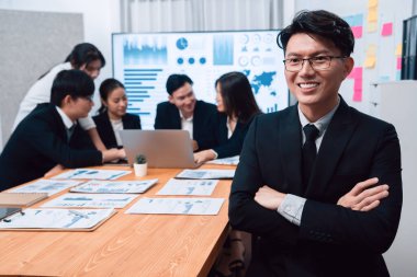 Focus portrait of successful confident male manager or executive in business wear with blurred background of businesspeople, colleagues working with financial report papers in office of harmony.