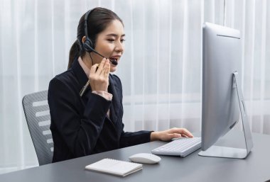 Bilgisayarında mikrofon ve kulaklıkla Asyalı çağrı merkezi çalışıyor. Kadın operatör istisnai müşteri hizmetleri sunar. Destek veren çağrı merkezi ajanı, müşteriye soruşturmada yardım ediyor. Coşkulu.