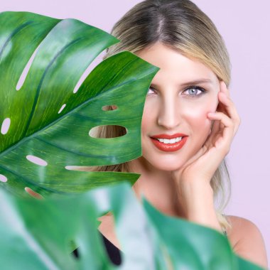 Mükemmel ciltli, yakın plan bir kadın ve yeşil canavarı elinde tutan kusursuz, yumuşak bir yüz makyajı. Doğal cilt bakımı güzellik veya pembe izole arka planda spa konsepti.