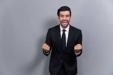 Siyah takım elbise giymiş heyecanlı ve mutlu iş adamı, başarılı bir iş tanıtımı, enerji ve neşe sonrasında, münzevi bir arka planda kutlama jesti olarak kolunu kaldırdı. Coşkulu