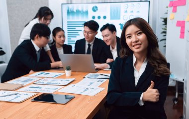 Focus portrait of female manger, businesswoman in the harmony meeting room with blurred of colleagues working together, analyzing financial paper report and dashboard data on screen in background.