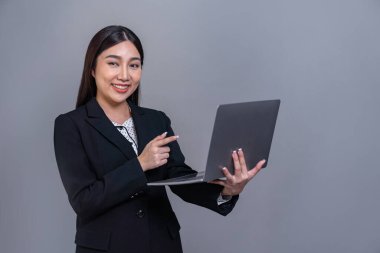 Özgüvenli genç Asyalı iş kadını dizüstü bilgisayarla izole edilmiş arka planda poz veriyor. Ofisteki kadın terfi satışları, teknoloji reklamları ya da insan kaynakları için el ele tutuşmalar yapıyor. Sevinçli.