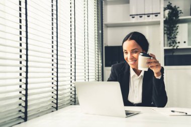 Competent female employee sits at her desk with a cup of coffee. Modern employee working with a drink, recreation during working hours, caffeine for people who are working