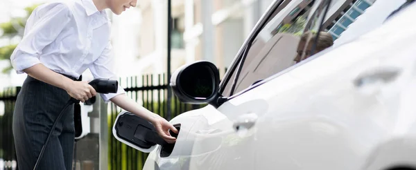 Closeup Progressive Businesswoman Smartphone Leaning Electric Car Charging Station Driving — Foto de Stock