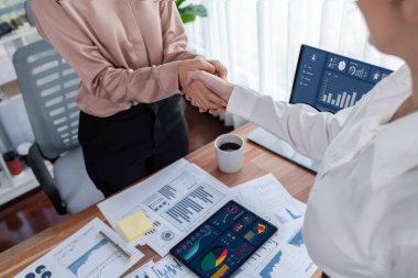 İki Asyalı iş kadını, iş yeri konseptinde takım çalışması ve dürüstlüğün önemi olarak, gösterge paneli veri kağıtlarının yığınlarını başarıyla analiz ettikten sonra modern ofiste el sıkışıyor. Coşkulu.