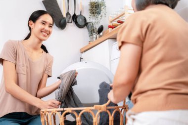 Daughter and mother working together to complete their household chores near the washing machine in a happy and contented manner. Mother and daughter doing the usual tasks in the house.