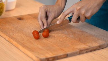 Close up hands holding a knife preparing a contented meal. Sliced tomatoes and other vegetables on the glass dish.