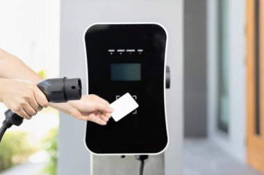 Hand holding credit card to pay public charging station and recharge her electric vehicle, symbolizing progressive lifestyle, combines e-wallet technology and sustainable transportation option.