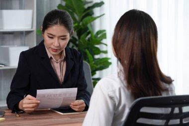 İki Asyalı kadın ofiste iş görüşmesi yapıyor. Başvuranlar özgeçmişi ve iş başvurusu hakkında konuşurken resmi takım giyerler. Muhabir olumlu ve konuşkan bir şekilde sorgulama talep ediyor. Coşkulu.