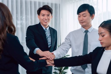 Closeup business team of suit-clad businessmen and women join hand stack together and form circle. Colleague collaborate and work together to promote harmony and teamwork concept in office workplace.
