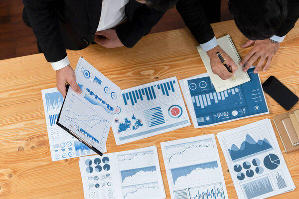 Top view analyst team discussing financial data on digital dashboard, analyzing chart and graph papers by data science software on wooden table background. Business intelligence and Fintech. Fervent