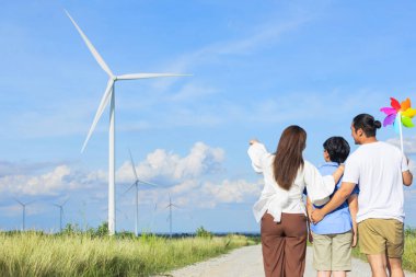 İlerici mutlu aile kavramı rüzgâr türbini çiftliğinde eğleniyor. Rüzgar türbini jeneratörüyle gelen elektrik jeneratörü kırsal bölgede tepe ve ufukta dağ var..