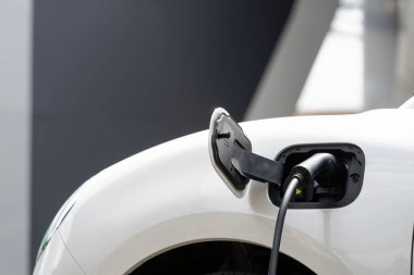 Closeup electric vehicle plugged-in with cable from charging point powered for progressive concept by alternative clean energy rechargeable EV car at home charging station.
