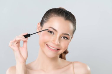 Closeup woman with blond hair putting glamorous black mascara with brush in hand on long thick eyelash. Perfect soft natural cosmetic makeup clean facial skin young woman in isolated background.