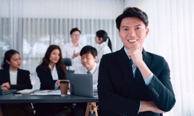 Portrait of focus young successful confident male manager, executive wearing business wear in harmony office arm crossed with blurred meeting background of colleagues, office worker.