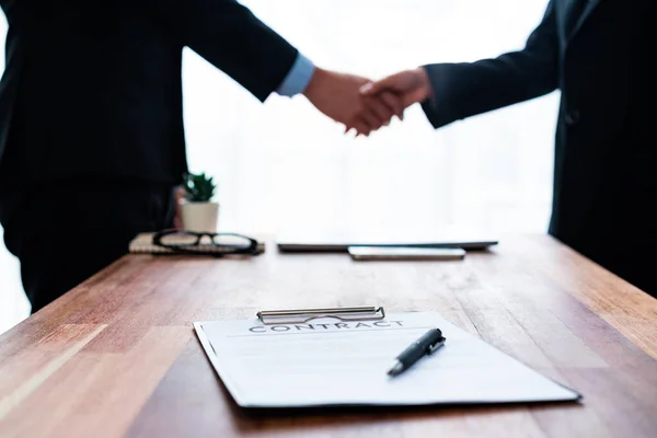Focus table top view of contract document on meeting table with blur background of business people shake hand. Business partnership concept background with contract agreement in legal form. Jubilant