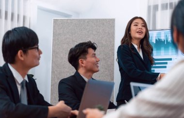 Confidence and young asian businesswoman give presentation on financial business strategy in dashboard report display on screen to colleagues in conference room meeting as harmony in workplace concept