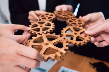 Yakın plan iş adamları el ele tutuşup mali raporlarla toplantı masasında bir araya gelirler. Çarkları sinerji uyum kavramı olarak tutan bir grup ofis çalışanı..