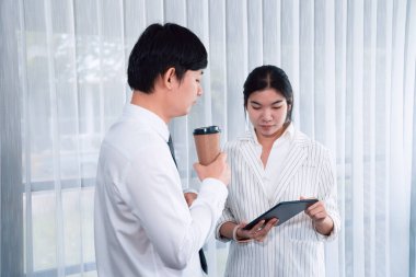 Manager advising guiding younger colleague with tablet in workplace. Couple businesspeople in formal wear working together on financial strategy as concept of teamwork and harmony in office.