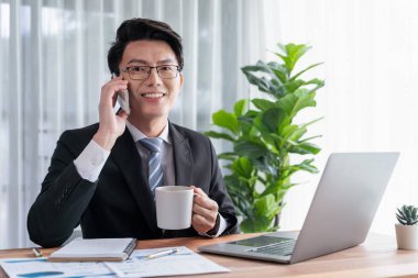 Ofis masasında akıllı telefonuyla bilgisayar başında çalışan bir iş adamı. Akıllı bir yönetici finansal iş verilerini araştırıyor ya da stratejik işler planlıyor, telefonla konuşuyor. Sevinçli.