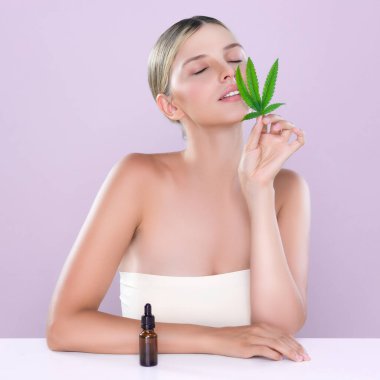 Cilt bakımı ürünleri için yeşil yaprak ve marihuana özlü şişe tutan pembe arka planda güzel bir kadının portresi. Kozmetik ve güzellik kavramları için kenevir CBD yağı.