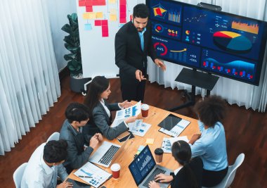 Modern toplantı odasındaki TV ekranında veri analizi paneliyle üst görünüm iş sunumu. İş adamlarının iş pazarlama stratejisini planlamak için beyin fırtınası yapması ya da birlikte çalışması. Uyum