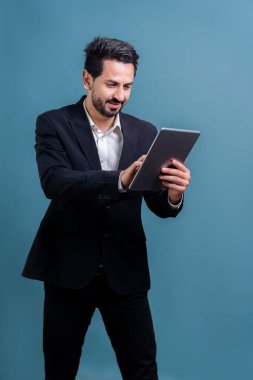 Resmi takım elbiseli kendine güvenen işadamı elinde tabletle sürpriz bir şekilde terfi ya da reklam arıyor. Yüz ifadeleri ve jestler, izole bir arkaplanda heyecan ve şaşkınlığa işaret ediyor. Coşkulu