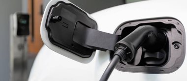 Closeup electric vehicle plugged-in with cable from charging point powered for progressive concept by alternative clean energy rechargeable EV car at home charging station.