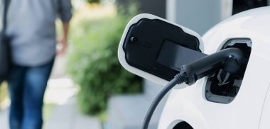 Focus electric car charging at home charging station with blurred progressive man walking in the background. Electric car using renewable clean for eco-friendly concept.