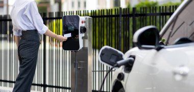 Credit card payment for eco-friendly clean and sustainable energy for electric vehicle at charging station. Progressive woman pay for charging point to power his electric rechargeable vehicle.