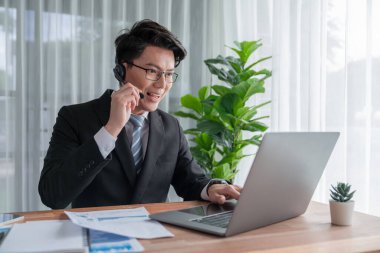 Kendine güvenen Asyalı telesales işadamı modern ofiste kulaklık takarak çalışır, müşterilere ve müşterilere online toplantıda BI gösterge paneli analizi sunar. Modern telesallerin başarısı. Sevinçli.