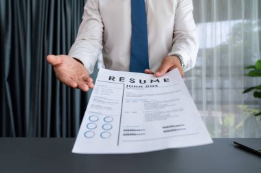 Resmi ofiste takım elbise giyen kendine güvenen bir adam, iş görüşmesi sırasında özgeçmiş kağıtlarını tutuyor. Röportajcı bakış açısına göre aday, özgeçmiş ödevini kamera önünde değerlendirmek üzere sunuyor. Coşkulu