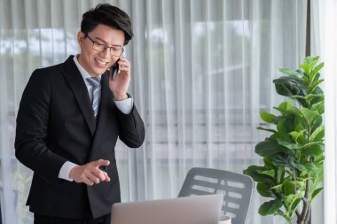 Ofis masasında akıllı telefonuyla bilgisayar başında çalışan bir iş adamı. Akıllı bir yönetici finansal iş verilerini araştırıyor ya da stratejik işler planlıyor, telefonla konuşuyor. Sevinçli.