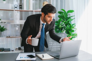 Modern ofis masasındaki modern profesyonel iş adamı elinde kahveyle çalışmak için dizüstü bilgisayar kullanıyor. Ofisinde bilgisayar defteri üzerinde çalışan çalışkan bir ofis çalışanı. coşkulu