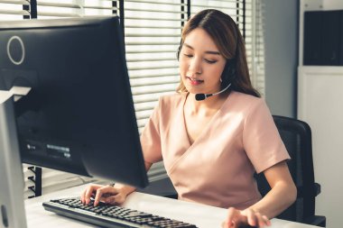 Competent female operator working on computer and while talking with clients. Concept relevant to both call centers and customer service offices.