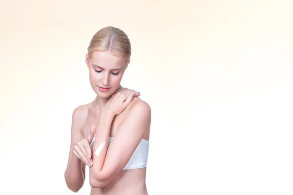 stock image Personable beautiful woman putting skincare moisturizer cream on her arm looking in camera in isolated background as concept for beauty care treatment. Female model applying lotion on her body.