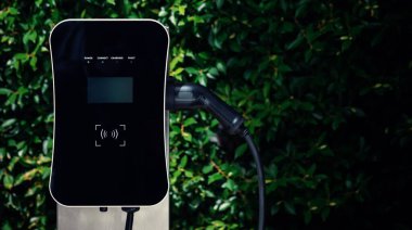 Charging station with greenery foliage background for combination of nature and alternative energy for progressive future renewable energy for electric car. Charger point with connecter device.