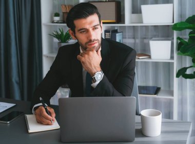Modern ofis masasındaki modern profesyonel iş adamı çalışmak ve notlar yazmak için dizüstü bilgisayar kullanıyor. Ofisinde bilgisayar defteri üzerinde çalışan çalışkan bir ofis çalışanı. coşkulu